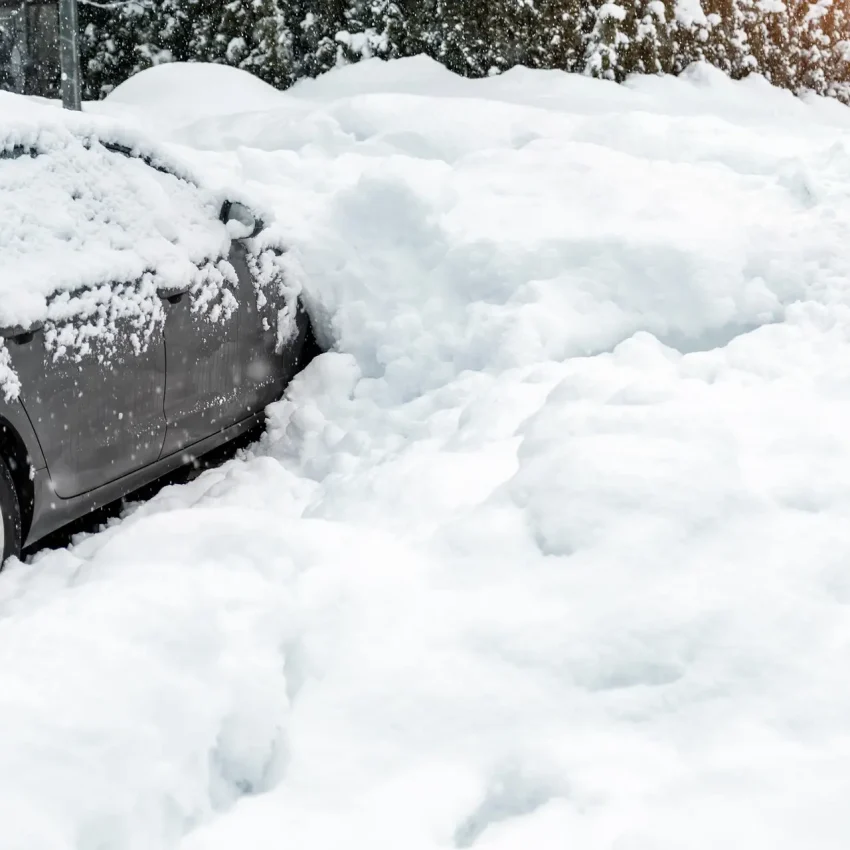 City street driveway parking lot spot with small car covered snow stuck trapped after heavy blizzard